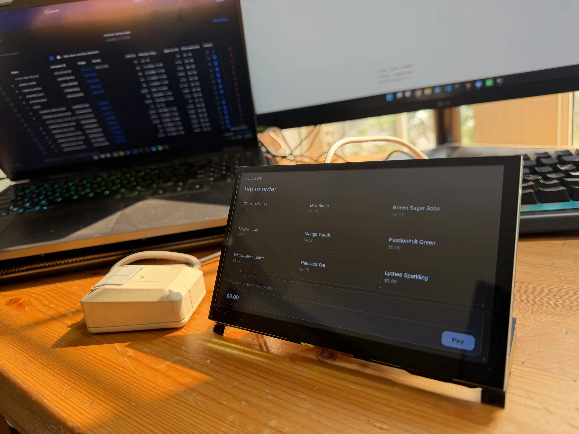 The practice's checkout unit on the bench: a single-board computer driving a small touchscreen showing a tap-to-order menu